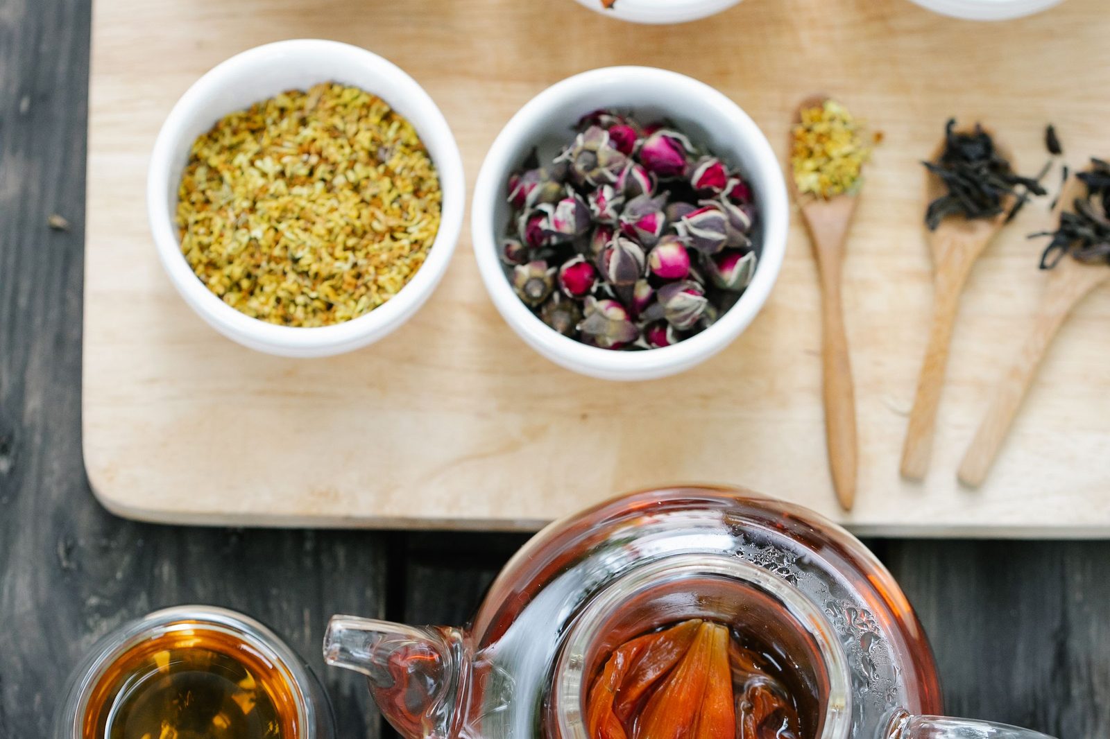 Dried herbs in small bowls with a pot of tea