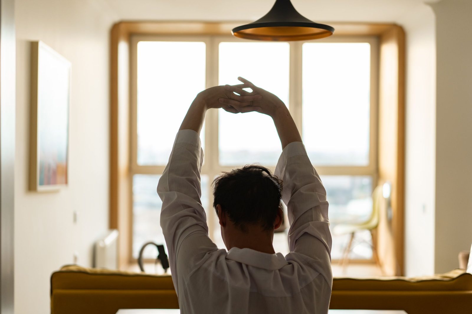 A man stretching by a sunny window in the morning